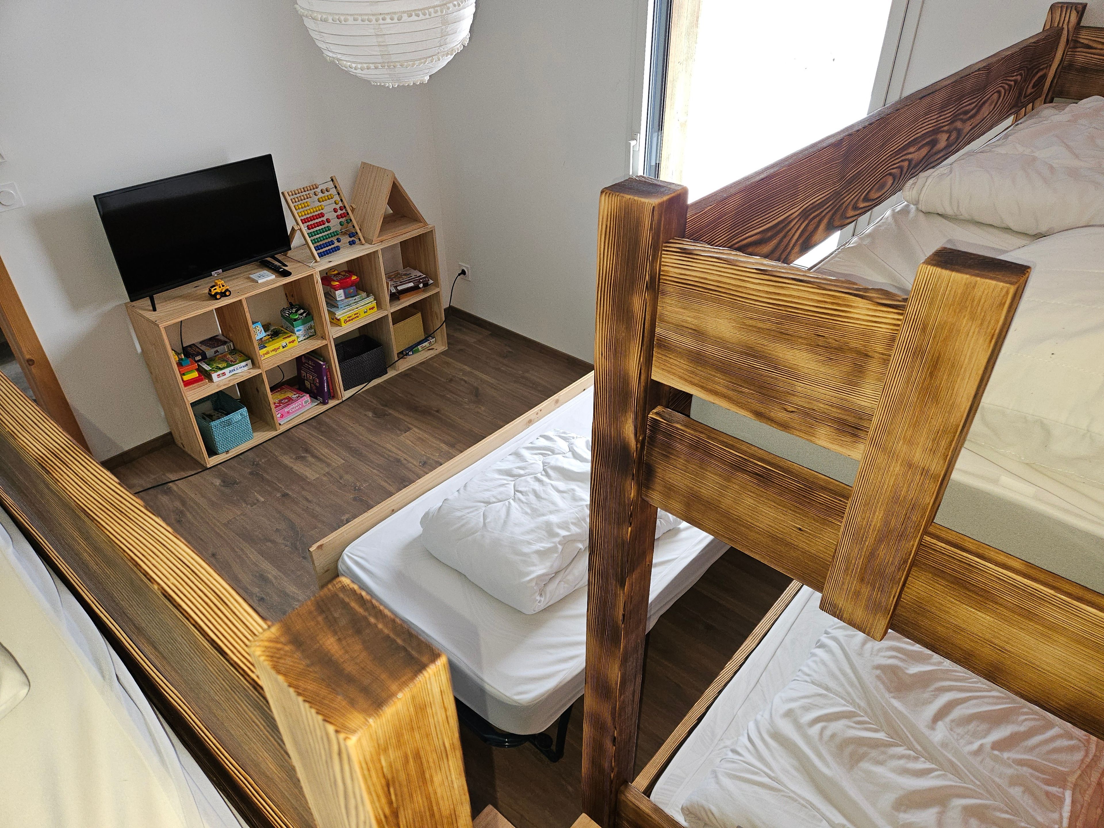 Ein Zimmer mit einem Etagenbett, einer Holzhockerkommode mit diversen Gegenständen und einem Fernseher.