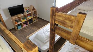 Ein Zimmer mit einem Etagenbett, einer Holzhockerkommode mit diversen Gegenständen und einem Fernseher.