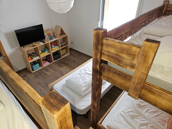 A room with a bunk bed, a wooden shelf unit with various items, and a television.