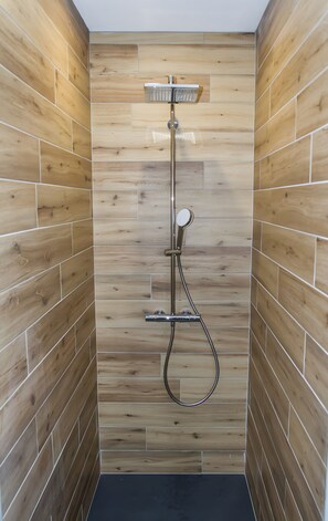 Eine Dusche mit Holzwand, Handbrause und Wandarmatur.
