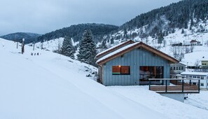 Eine Holzhütte mit einem Balkon, umgeben von schneebedeckten Hügeln und Bäumen.