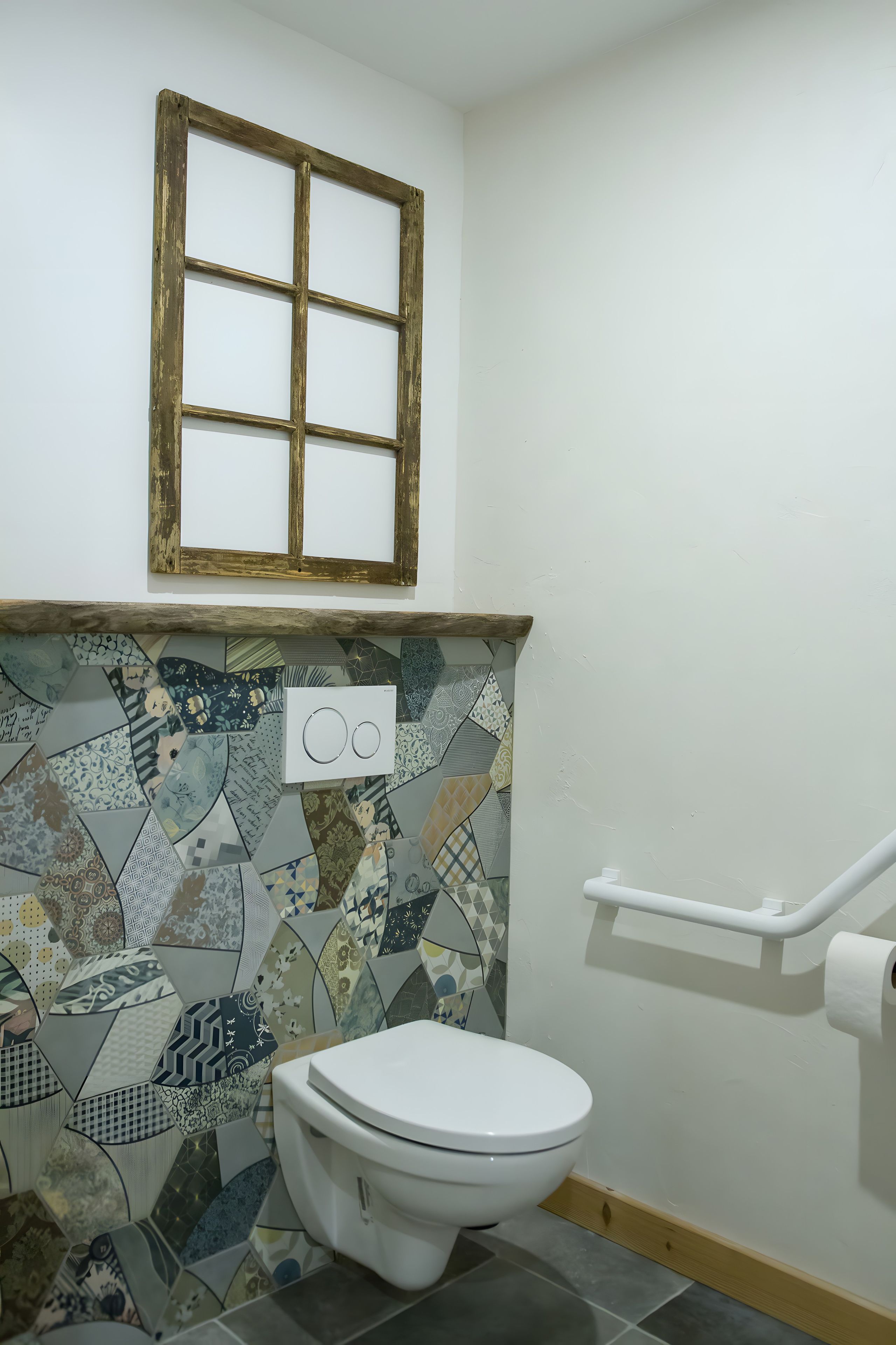 Une salle de bain avec des toilettes, un mur décoré d’un motif, une fenêtre et une barre d’appui.
