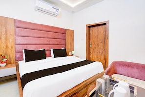 A hotel room with a bed, a wooden headboard, a wooden door, a nightstand, a lamp, and a chair.