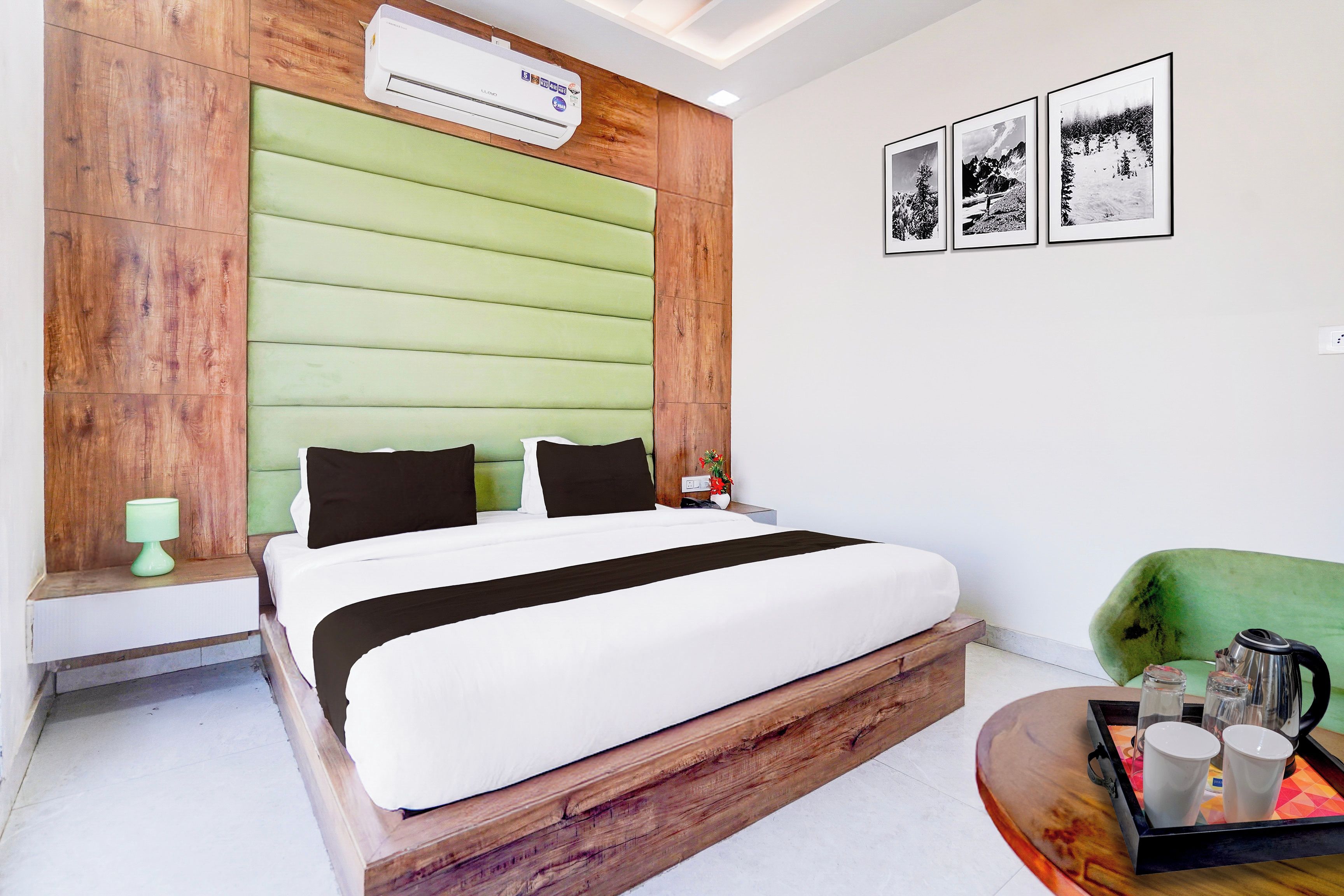 A hotel room with a bed, a green upholstered headboard, a wall-mounted air conditioner, and framed pictures.