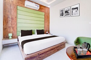 A hotel room with a bed, a green upholstered headboard, a wall-mounted air conditioner, and framed pictures.