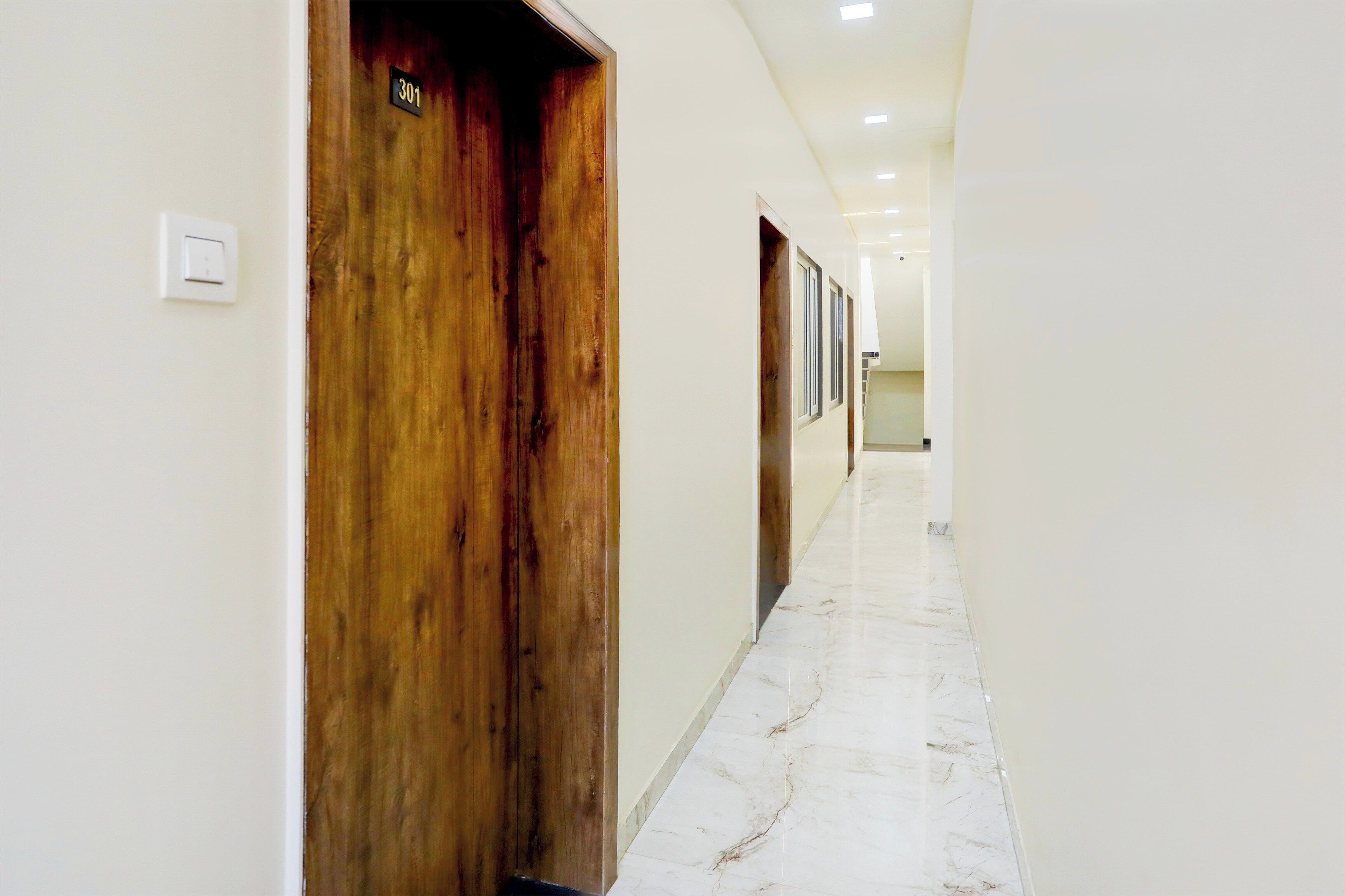 A hotel corridor with wooden doors, white walls, and marble flooring.