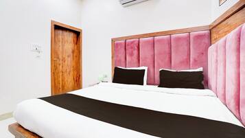 A bedroom with a bed, a wooden door, an air conditioning unit, and a nightstand with a lamp.