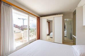 Ein Hotelzimmer mit einem großen Bett, einer Schiebetür, die auf einen Balkon führt, und einem Badezimmer mit einer Dusche.