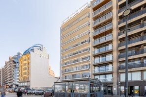 Ein mehrstöckiges Gebäude mit Balkonen, einem Café im Erdgeschoss und einem wolkenlosen Himmel.