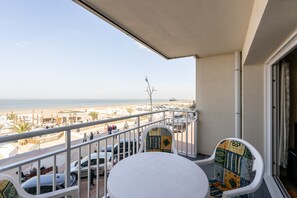 Ein Balkon mit Blick auf den Strand, einem Tisch, Stühlen und geparkten Autos.