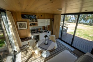 A cozy indoor space with a dining table, chairs, a sofa, a kitchen area, and a large sliding glass door leading to an outdoor deck. - Stunning Tiny House by Lake Tawakoni for a Peaceful Glamping Getaway near Quinlan, Texas (Quinlan)