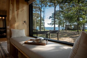 A room with a large window overlooking a beach and trees, a wooden bench, and a tray with a teapot and cup. - Stunning Tiny House by Lake Tawakoni for a Peaceful Glamping Getaway near Quinlan, Texas (Quinlan)