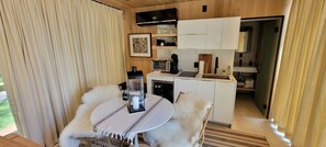 Um quarto aconchegante com uma mesa redonda, uma cadeira branca, uma máquina de café e uma pequena cozinha compacta.