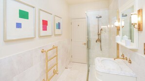 Un baño con cabina de ducha de vidrio, un perchero dorado y cuadros en la pared.