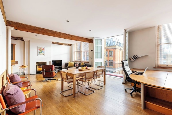 A spacious living area with a wooden dining table, comfortable seating, a fireplace, and a view of the city through large windows.