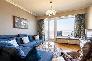 A living room with a blue sofa, a coffee table, and a view of the outdoors. - Apartment in Blankenberge by the Pier (Blankenberge)