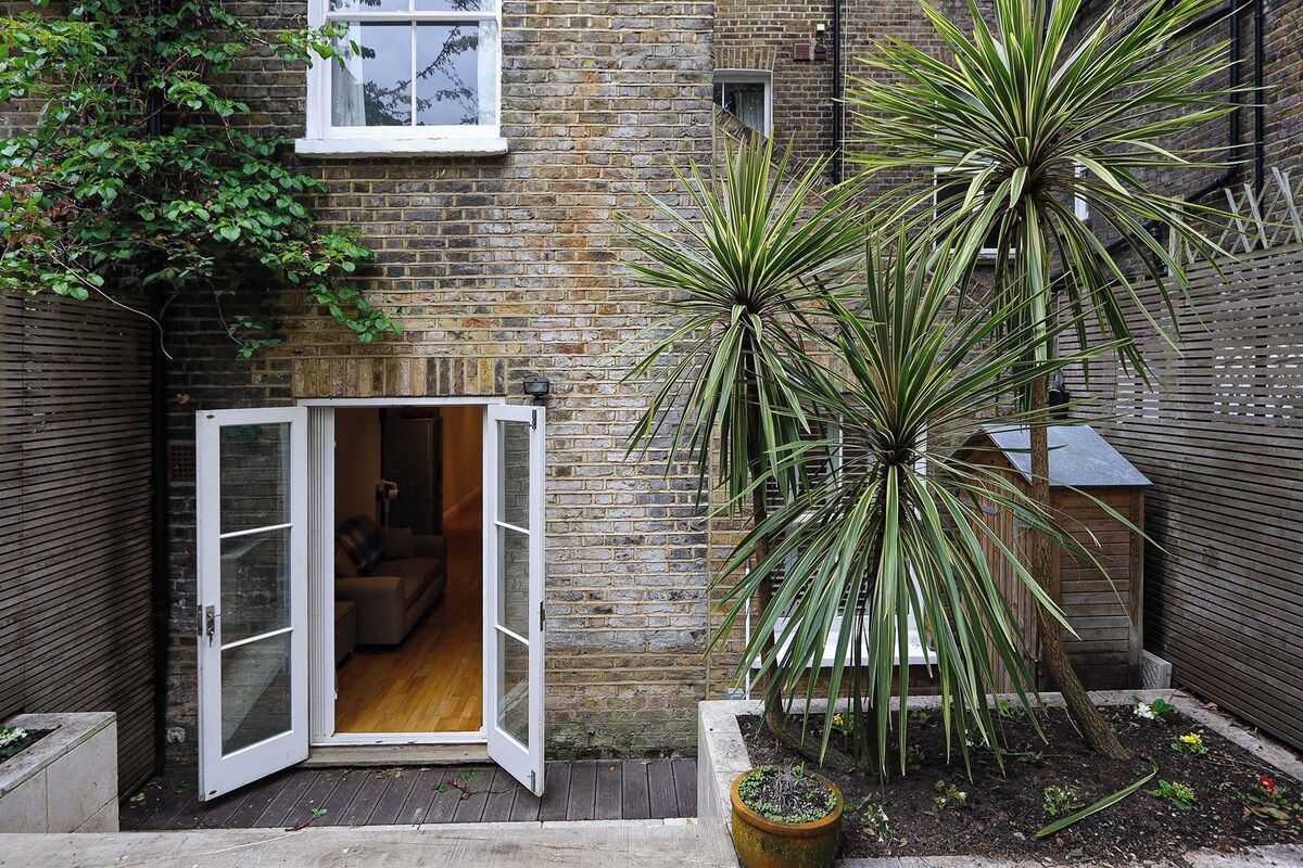 Un bâtiment en briques avec une porte en bois donnant sur un espace intérieur, une plante en pot et un petit jardin.