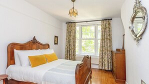 Un dormitorio con cama de madera, una mesita de noche, un aparador, una ventana con cortinas y una lámpara colgante.