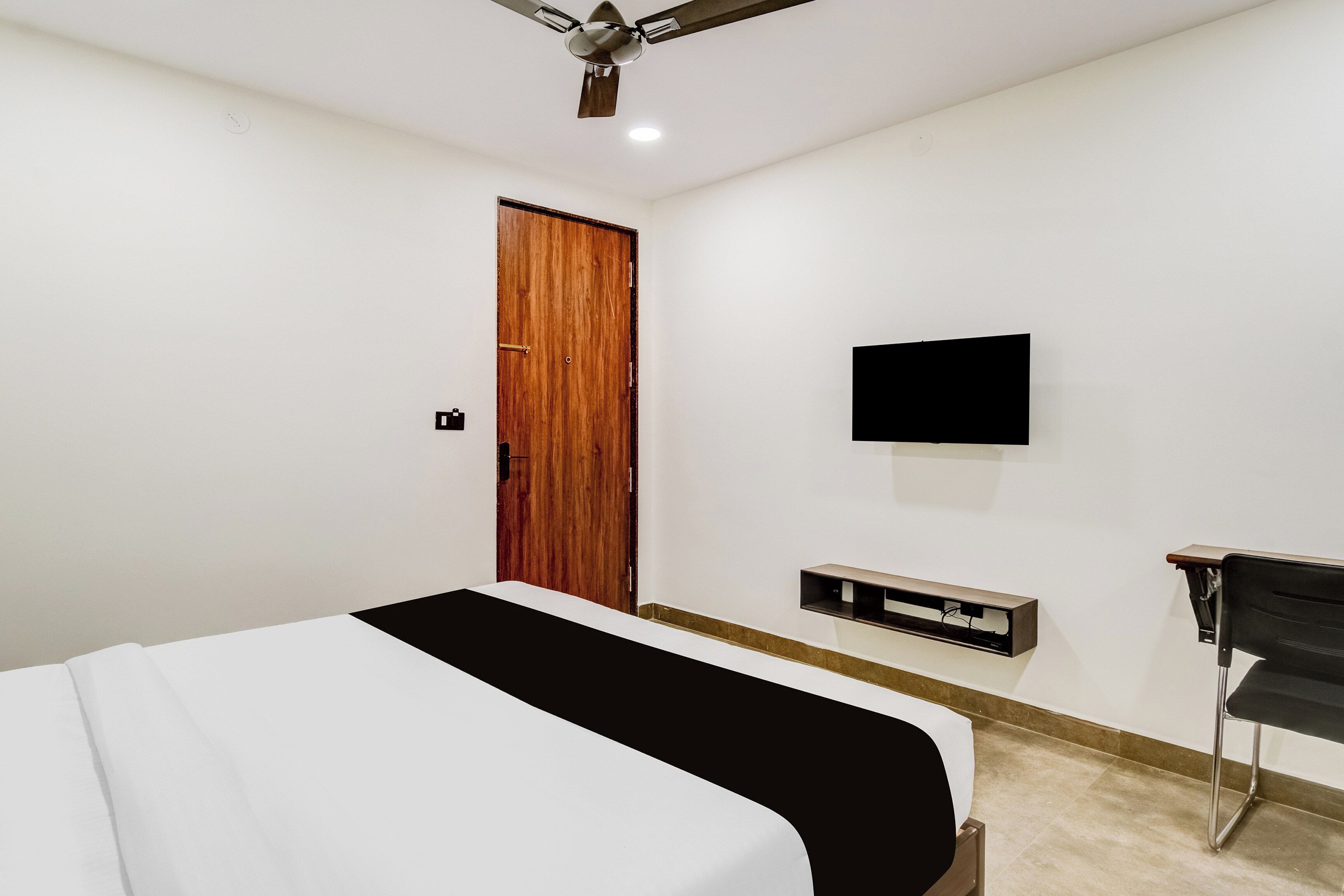 A bedroom with a bed, a television mounted on the wall, and a desk with a chair.