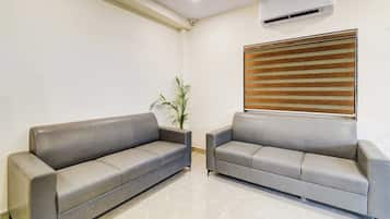 Dos sofás grises en una habitación con pared blanca, una planta en maceta y una ventana con persianas.