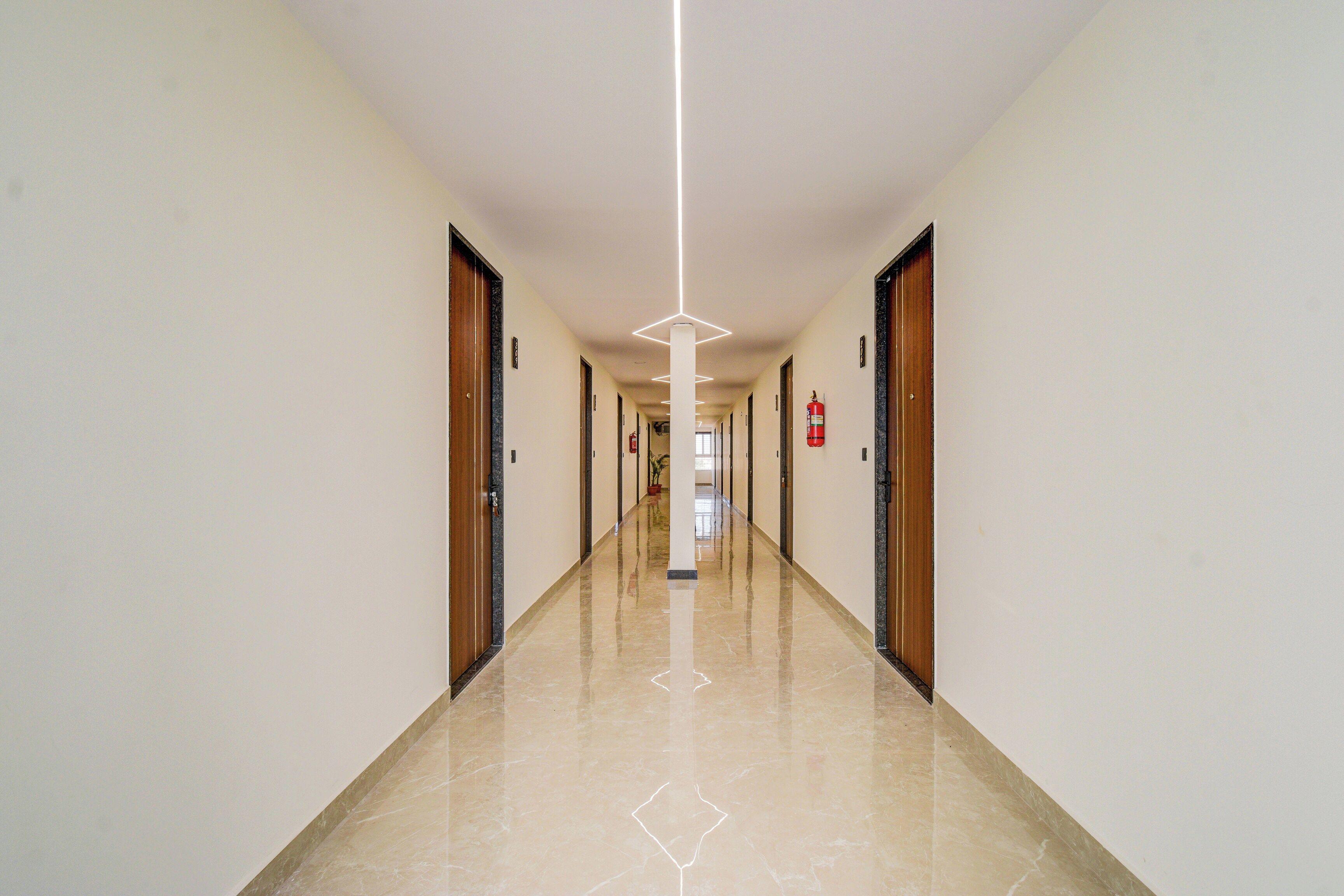 A long, narrow hallway with doors on both sides, a fire extinguisher mounted on the wall, and a clean, polished floor.