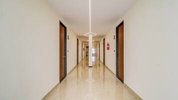 A long, narrow hallway with doors on both sides, a fire extinguisher mounted on the wall, and a clean, polished floor.