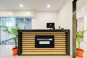 Un mostrador de recepción con un cartel que dice 'TOWNHOUSE OAK' y 'Servicio de empresa'. Hay plantas en macetas a ambos lados del mostrador.