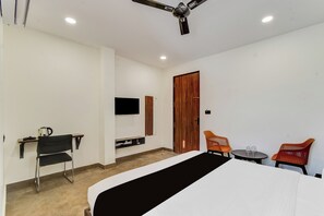 Una habitación de hotel con cama, escritorio, silla, televisor y ventana con cortinas.
