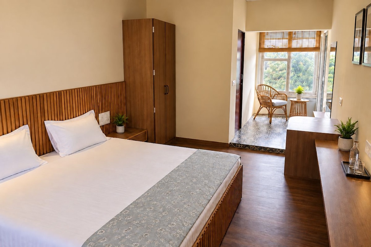Quarto de hotel com uma cama grande, armário de madeira e um pequeno espaço de estar com mesa e cadeiras.
