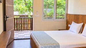 Een slaapkamer met een houten bed, een bankje en uitzicht op een houten terras en groen.