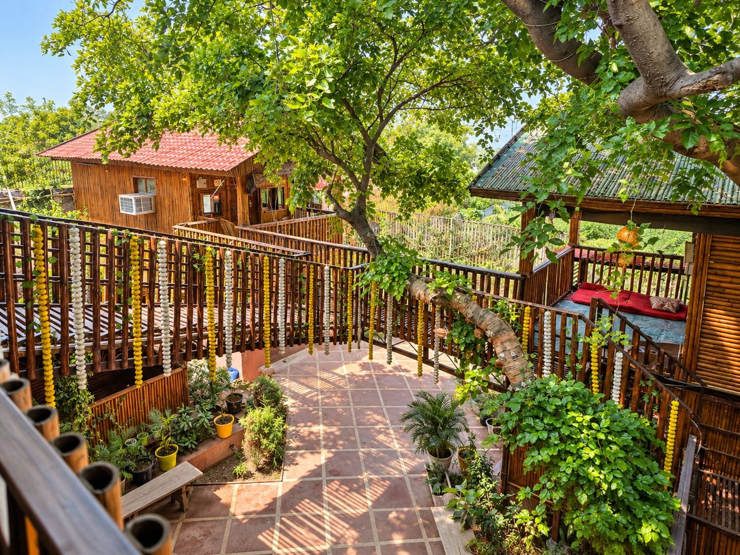 A wooden house with a red roof, surrounded by a bamboo fence and potted plants.