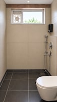 Un baño moderno con inodoro, ducha con cabezal de ducha manual y una ventana sobre la ducha.