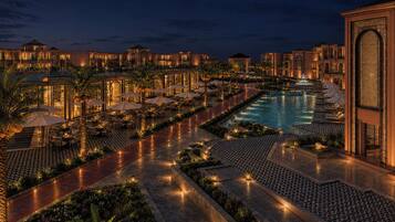 Vista nocturna de un hotel con piscina, mobiliario exterior y senderos bien iluminados.