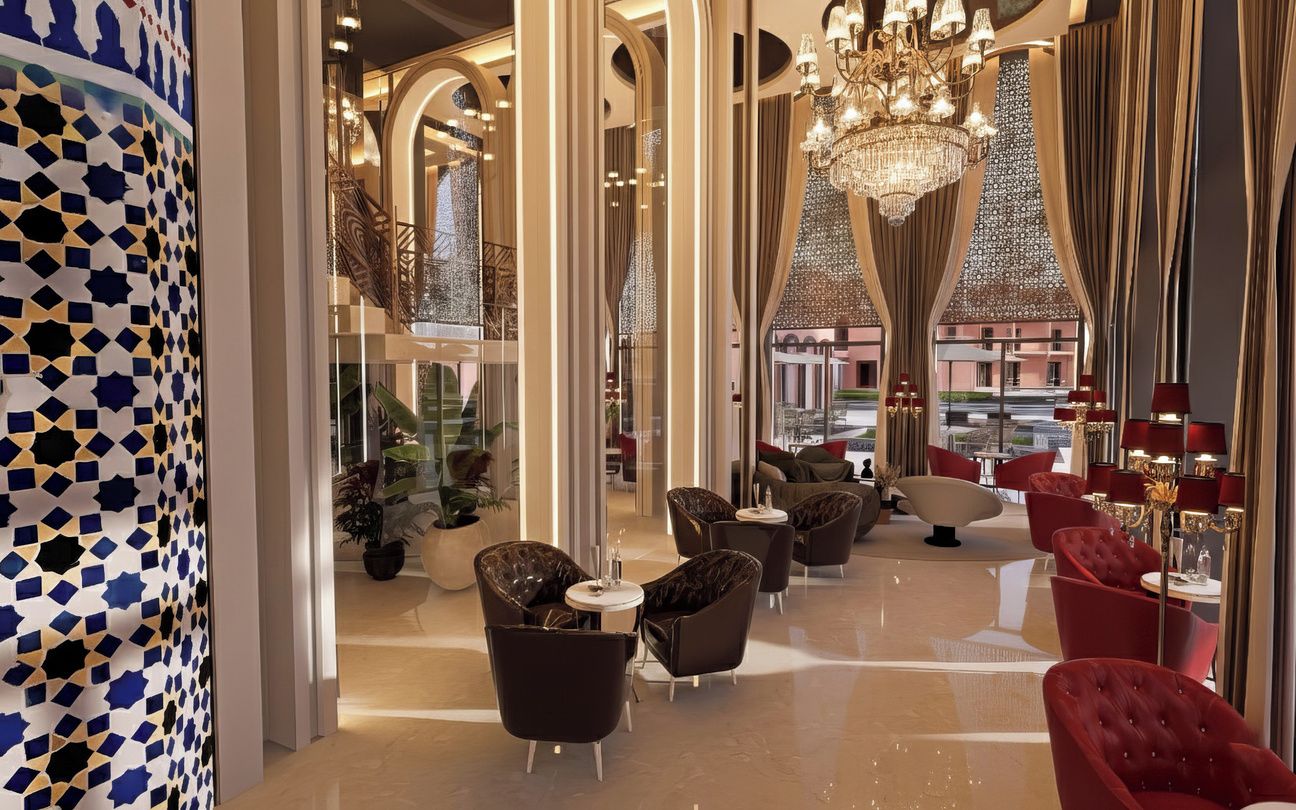 Vestíbulo de hotel con diseño moderno, que presenta una araña, sillas tapizadas en rojo y negro, y un revestimiento de pared con estampado.
