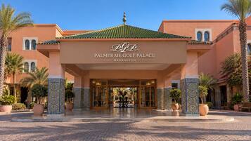 Der Eingang des Palmiera Golf Palace mit einer gefliesten Fassade, Palmen und blauem Himmel.