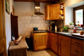 Cozinha com armários de madeira, fogão a gás, coifa de aço inoxidável e janela que permite entrada de luz natural.
