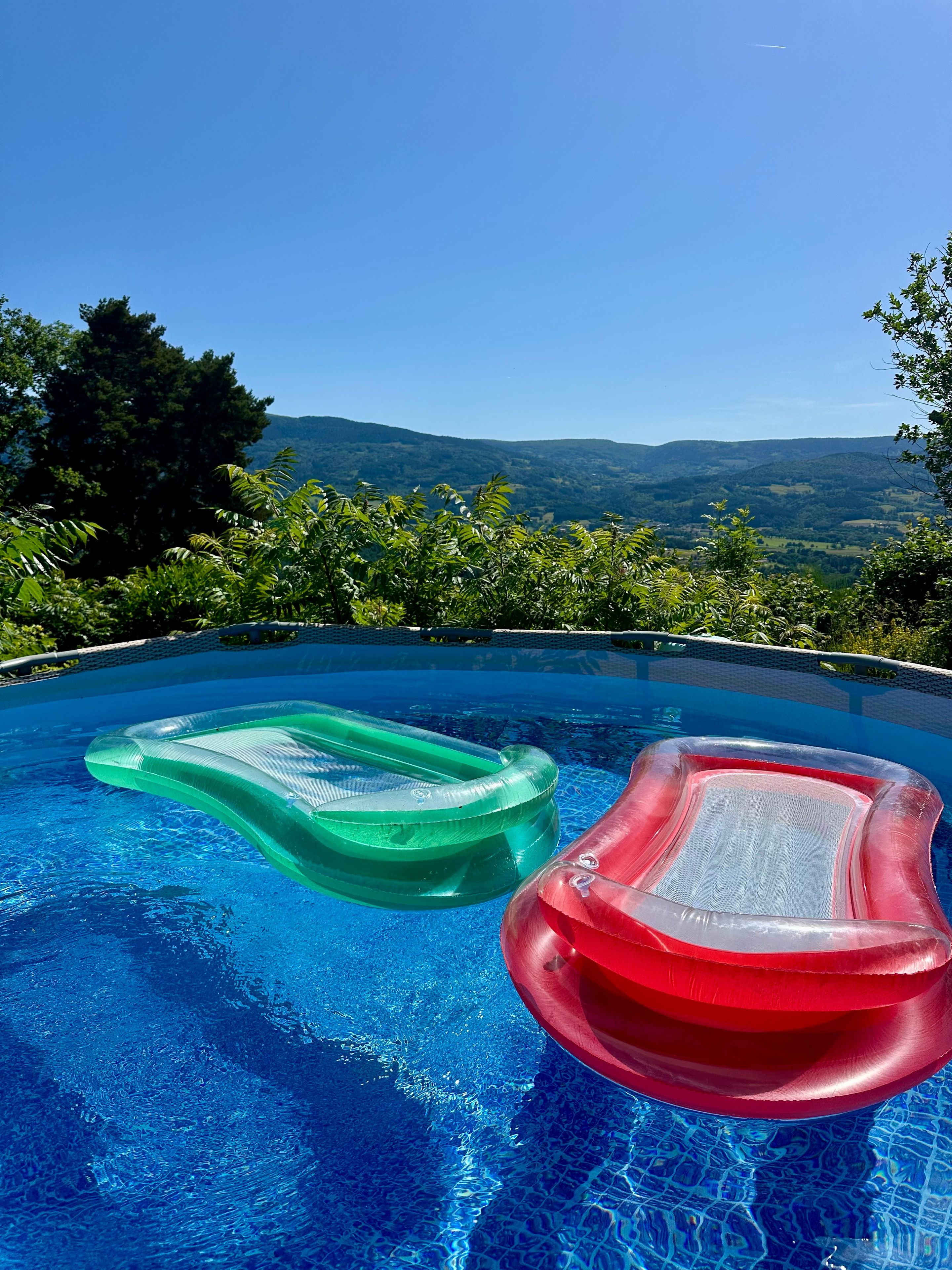 Une piscine à débordement avec deux matelas gonflables, entourée d’une végétation luxuriante et offrant une vue imprenable sur les montagnes.