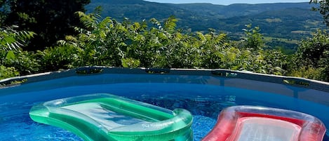 An infinity pool with two inflatable loungers, surrounded by lush greenery and a mountainous backdrop.