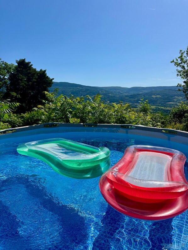 An infinity pool with two inflatable loungers, surrounded by lush greenery and a mountainous backdrop.