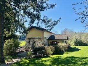A small stone building with a tiled roof, surrounded by greenery and trees.