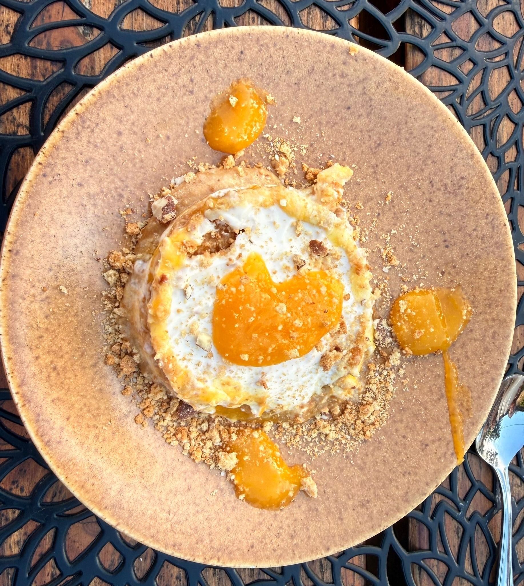 A round plate with a dessert featuring a poached egg, caramelized fruit, and crumbled topping.
