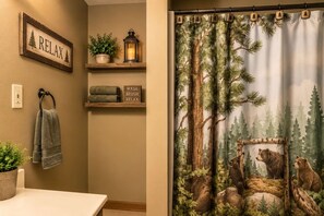 Ein Badezimmer mit Handtuchhalter, Ablagefläche mit Topfpflanze und Laterne sowie einem an der Wand befestigten Schild mit dem Wort 'RELAX'.