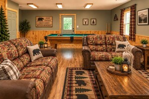 Ein gemütlicher Raum mit Billardtisch, zwei Ledersofas mit gemusterten Kissen, einem Holztisch und einem Kamin.