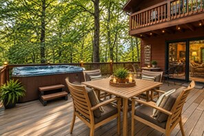 Una terraza de madera con un jacuzzi, mobiliario exterior y vistas al bosque.