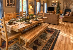 Ein Holztisch mit Bänken, ein Kamin und eine gemütliche Wohnarea mit Sofa und Weihnachtsbaum.