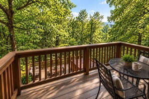 Eine Holzterrasse mit einem Metalltisch und -stühlen, umgeben von üppigen, grünen Bäumen.