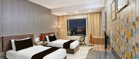 A hotel room with two beds, a desk, a chair, a TV, and a window with a city view.