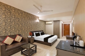 Habitación de hotel con cama, sofá, mesa de centro, aire acondicionado y kitchenette.