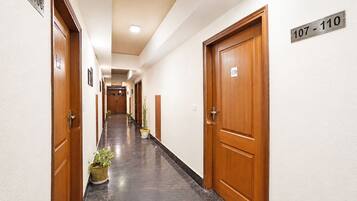 A hotel corridor with wooden doors, numbered room signs, and potted plants.