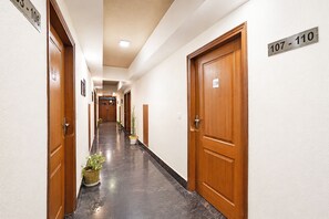 Un pasillo de hotel con puertas de madera, placas de números de habitación y plantas en macetas.